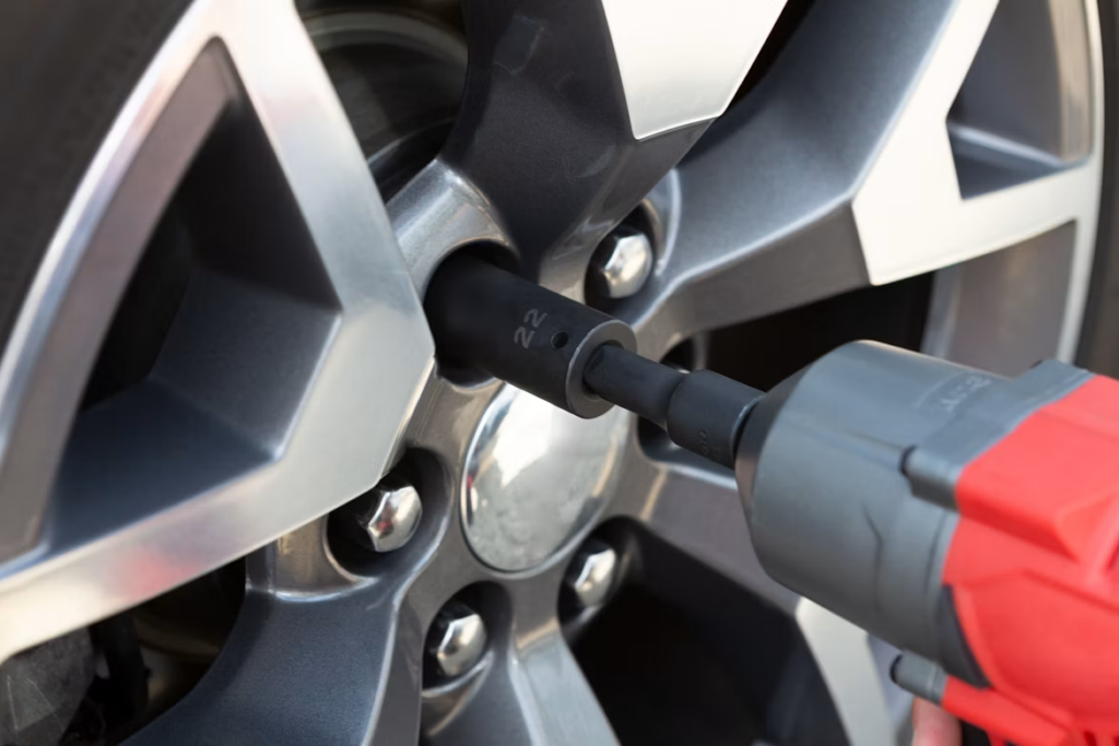 A technician using an impact wrench on a car wheel's lug nuts.