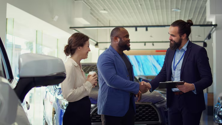 Log book service: salesperson shaking hands with couple at dealership.