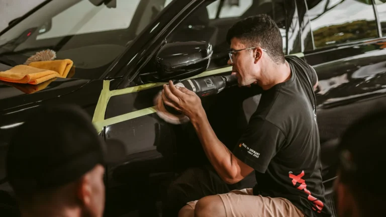 Log book service: detailer polishing black car mirror with buffer.