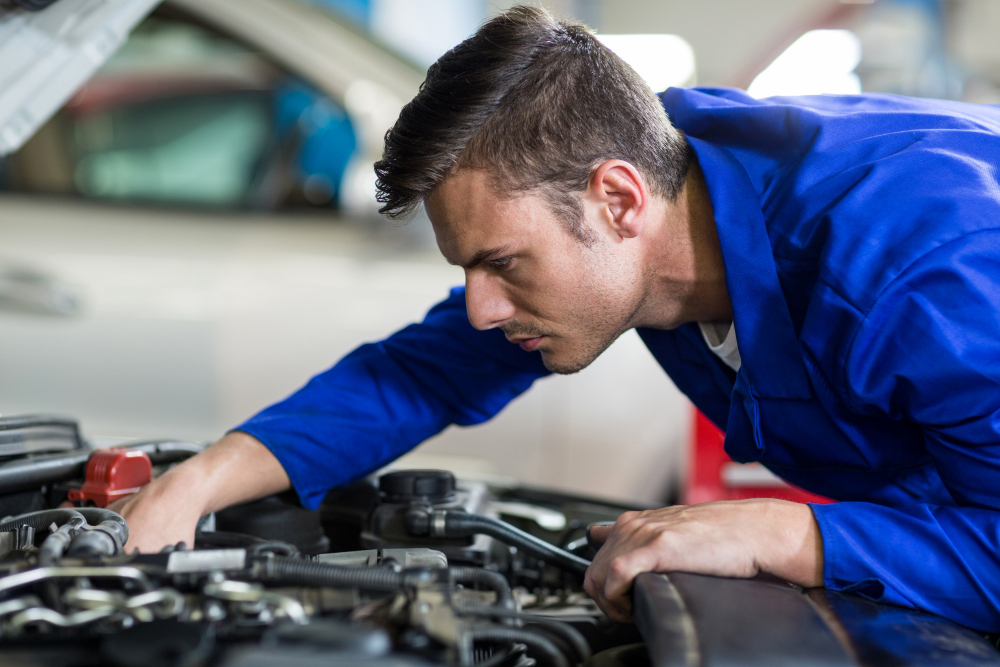 Mechanic checking a car engine bay for fluid leaks before a safety inspection

